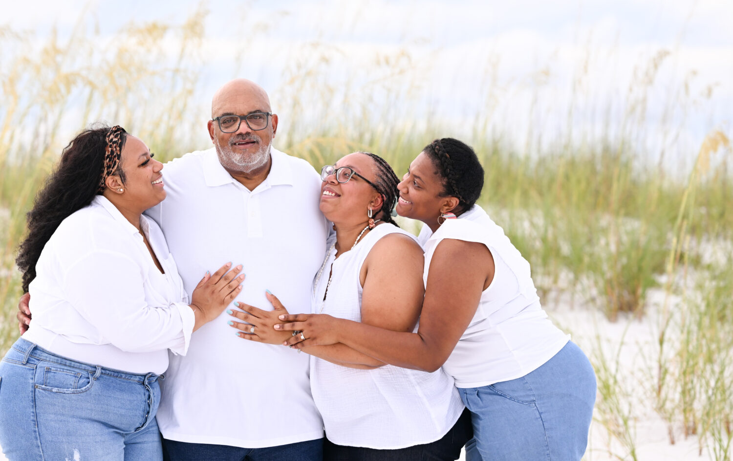 Dad and his a three daughters embracing on the beach.